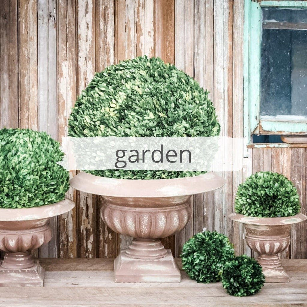 Grouping of garden urns with distressed rustic finish filled with balls of dried boxwood